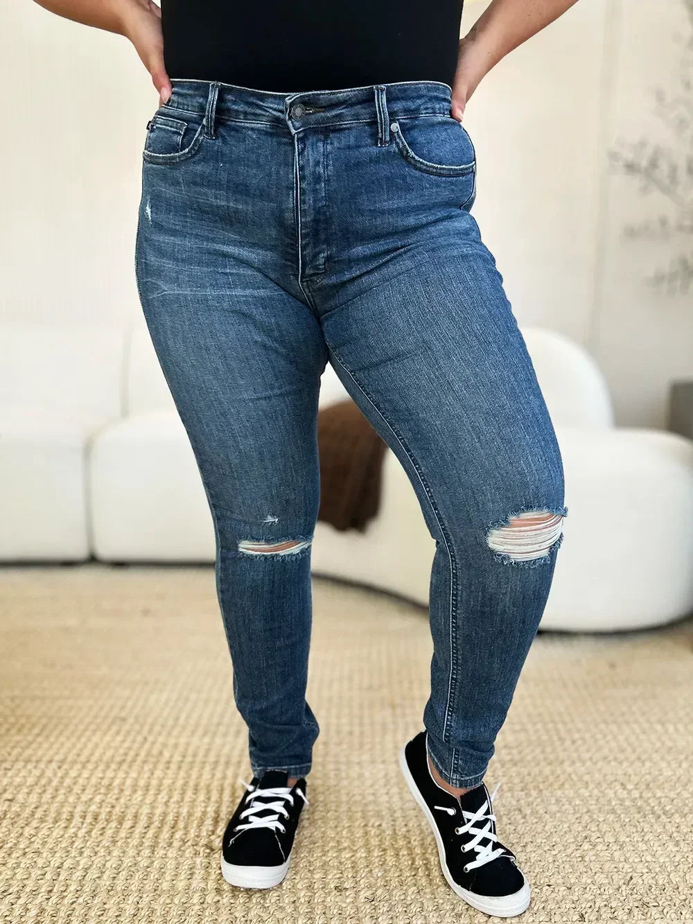 Woman wearing high-waisted distressed skinny jeans and black sneakers indoors