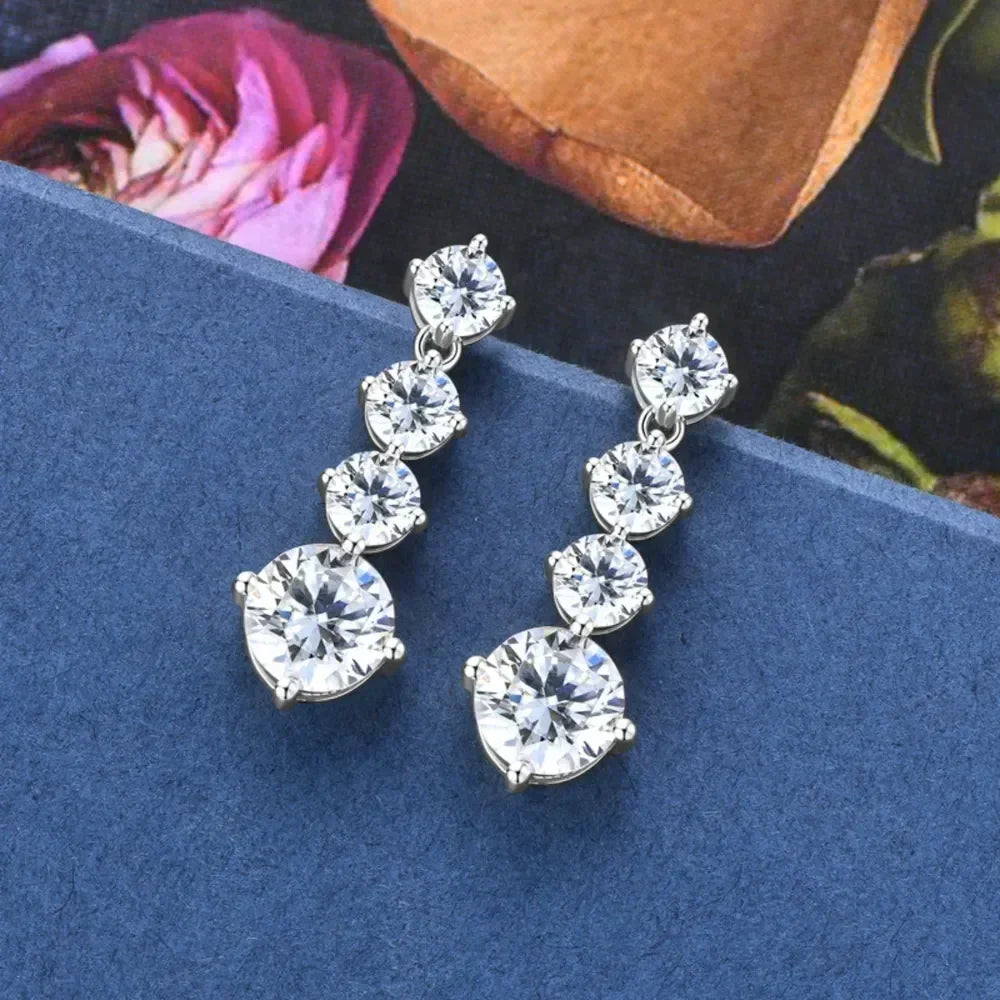 Elegant silver drop earrings with four round clear gemstones on a blue background