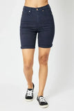 Woman wearing high-waisted dark denim Bermuda shorts with cuffed hems and black sneakers