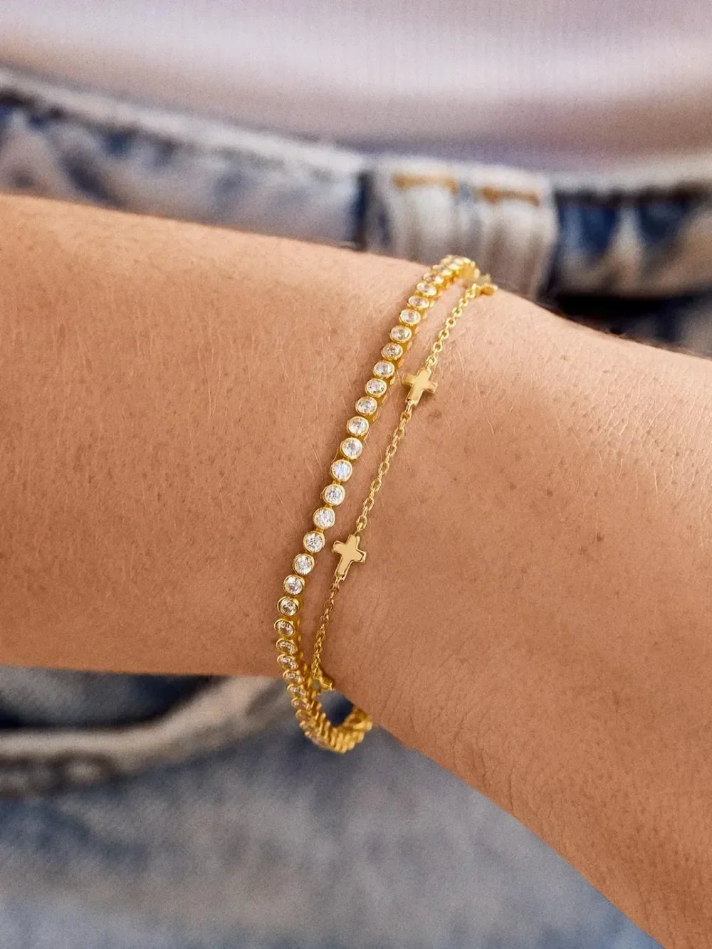 Gold layered bracelets with crystals and cross charm on woman's wrist, casual outfit