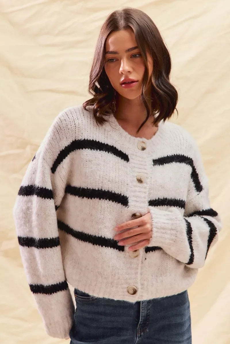 Woman wearing a cozy white knit cardigan with black stripes and button front, paired with jeans