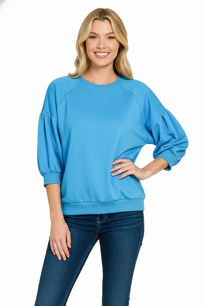 Woman wearing a blue puff sleeve sweatshirt with relaxed fit and dark skinny jeans on white background