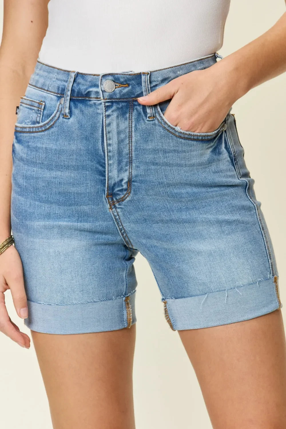 Woman wearing high-waisted, rolled hem denim shorts and a white ribbed tank top