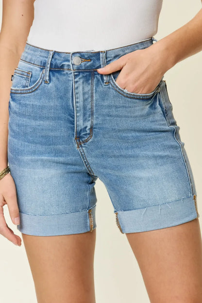 Woman wearing high-waisted, rolled hem denim shorts and a white ribbed tank top