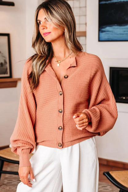 Woman wearing a ribbed, button-up, blush pink cardigan with balloon sleeves and white pants.