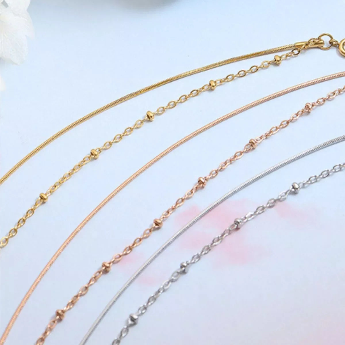 Minimalist gold, rose gold, and silver chain necklaces with delicate detailing on white background.