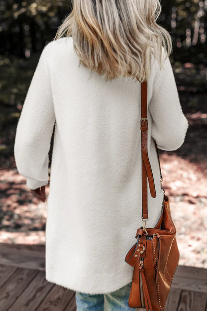 Woman in a cream textured sweater with a brown leather shoulder bag, outdoors.