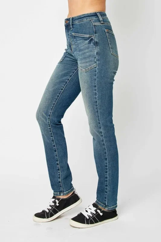 Woman wearing high-waisted straight leg blue jeans with front patch pockets and black sneakers