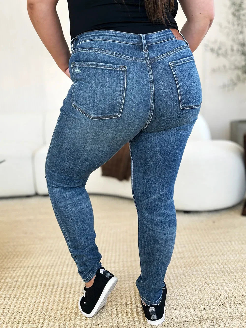 Woman wearing high-waisted blue skinny jeans and black sneakers indoors