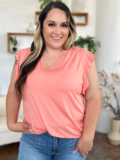 Woman in a peach flutter sleeve top and blue jeans standing in a bright, modern room