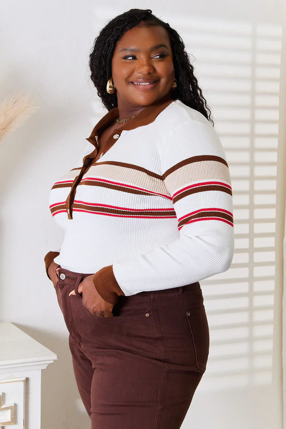 Woman wearing a white ribbed long sleeve polo with brown and red stripes, paired with high-waisted brown pants.