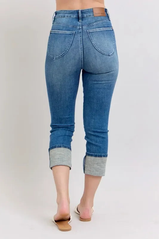Back view of woman wearing cuffed blue cropped jeans with large back pockets and flat sandals