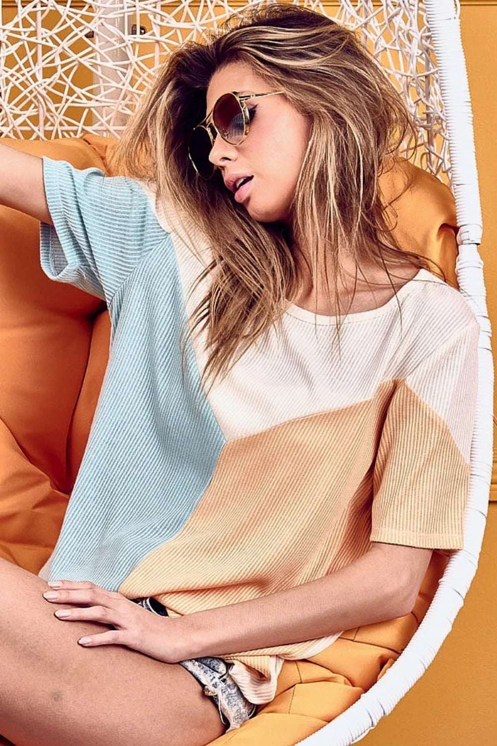 Woman in sunglasses wearing a relaxed, colorblock short sleeve top in a modern chair