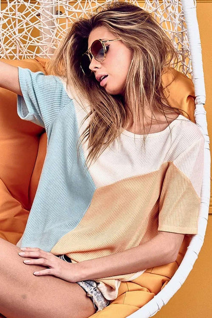 Woman in sunglasses wearing a relaxed, colorblock short sleeve top in a modern chair