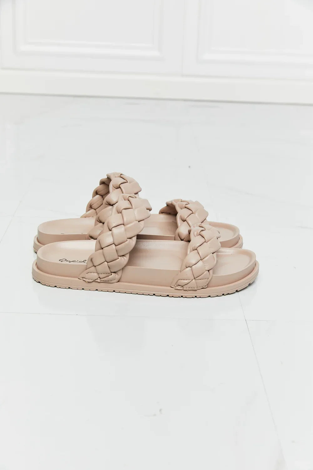 Beige braided double strap slip-on sandals on white tile floor