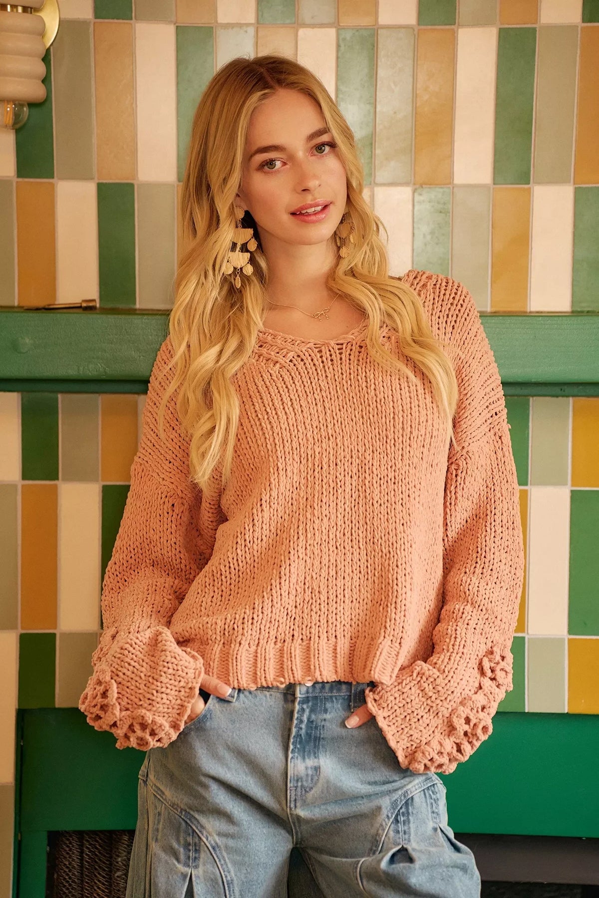 Woman in a loose knit blush pink sweater and light blue jeans, standing indoors