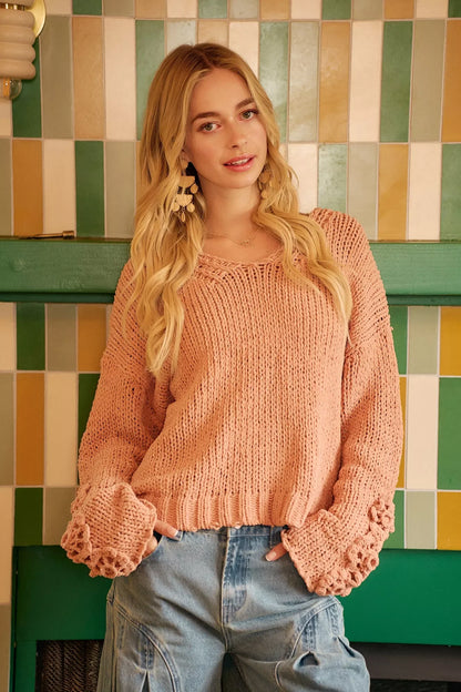 Woman in a loose knit blush pink sweater and light blue jeans, standing indoors