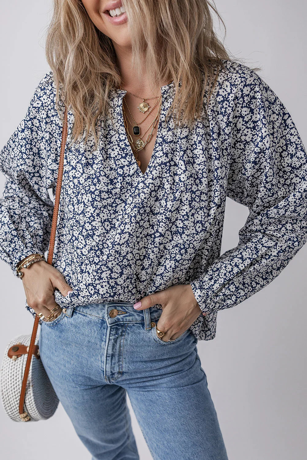Woman wearing a blue floral blouse with light wash jeans and layered gold necklaces