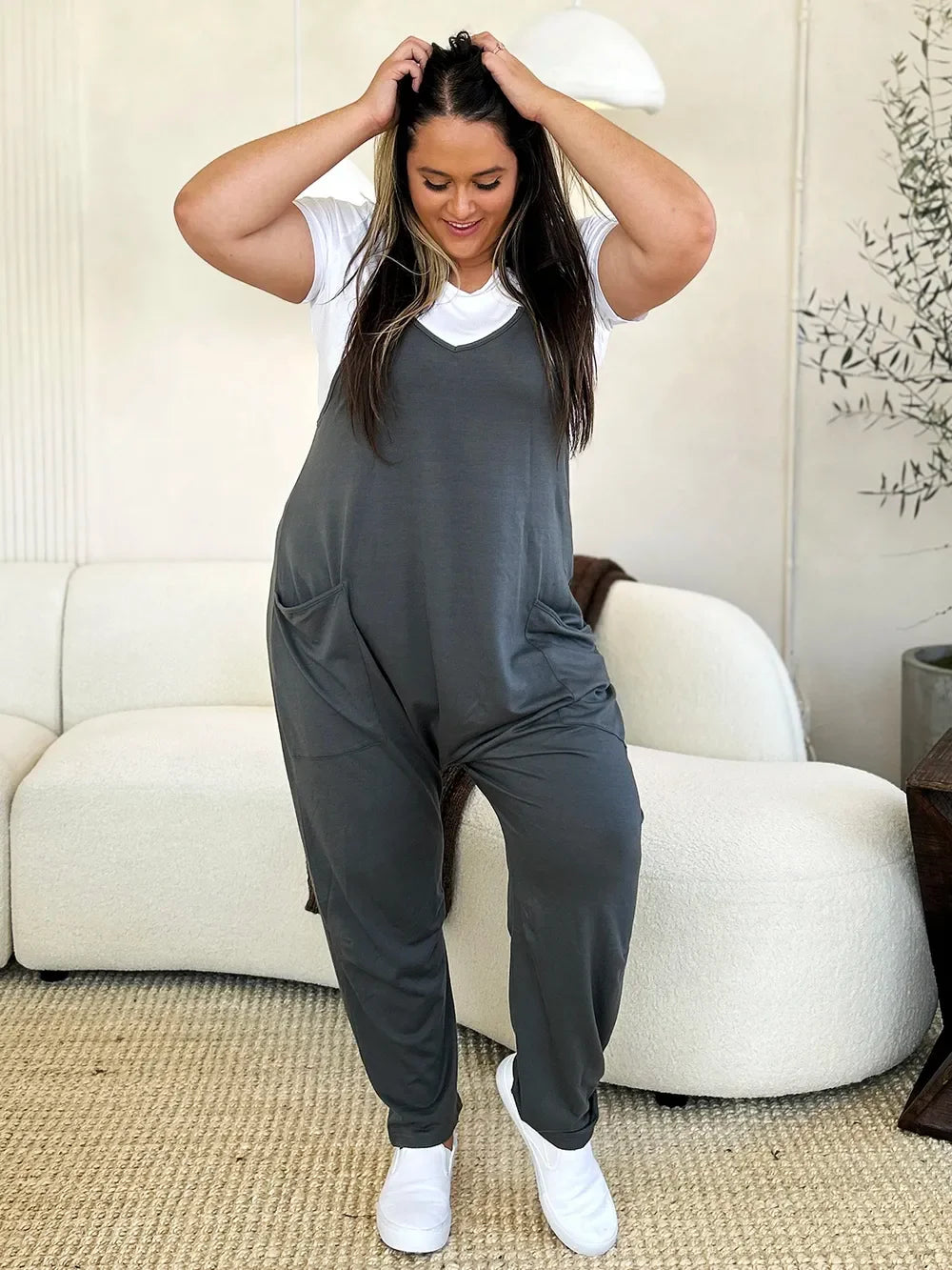 Woman wearing relaxed fit charcoal jumpsuit over white t-shirt, standing in modern living room