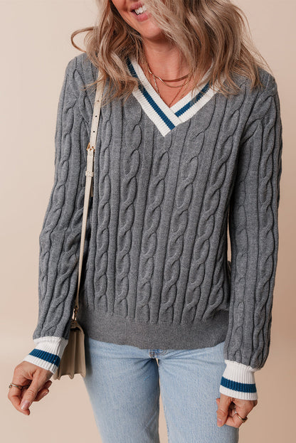 Person wearing a gray cable knit sweater with white and blue trim on a beige background