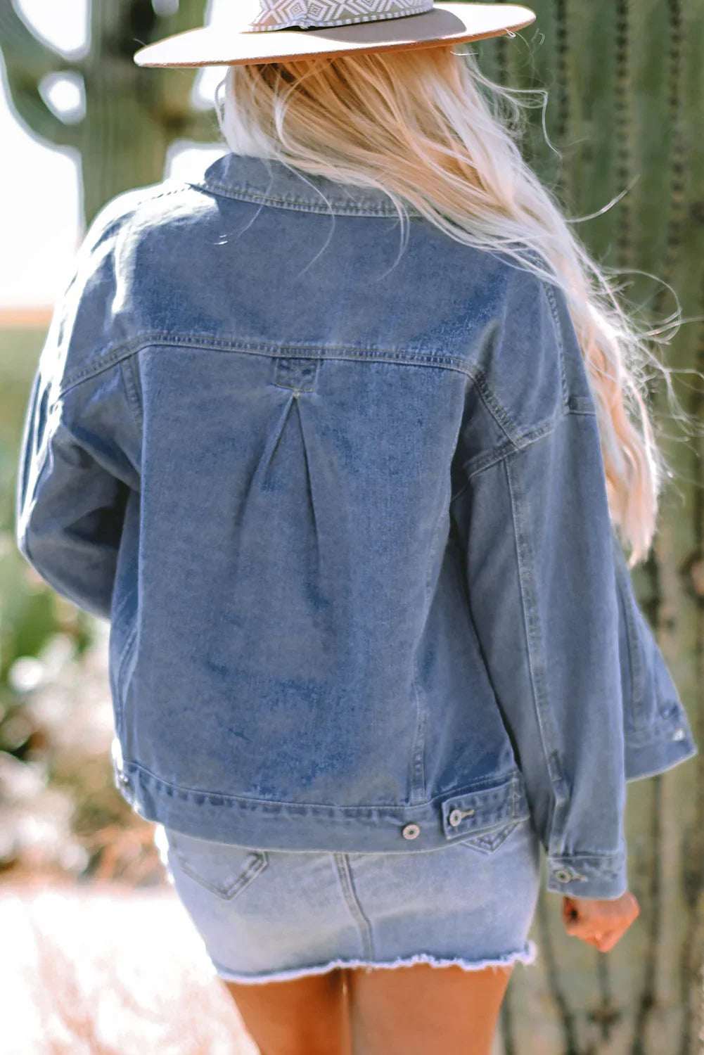 Woman wearing a denim jacket and skirt outdoors, with long blonde hair and a sun hat