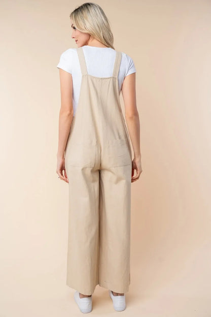 Woman in beige wide-leg overalls and white top, shown from the back, neutral background