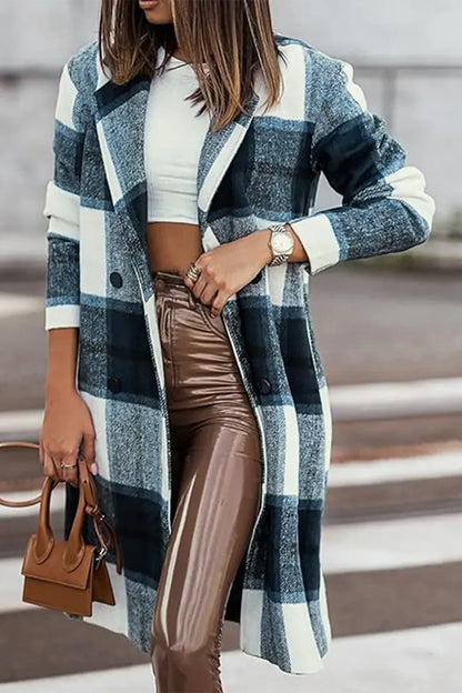 Woman wearing a blue plaid long coat, white crop top, brown shiny pants, and holding a small brown handbag