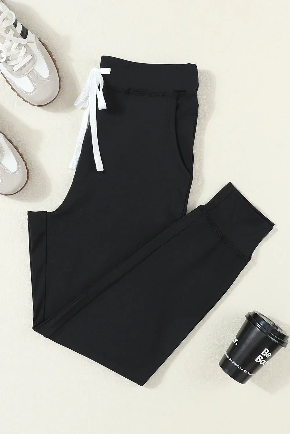 Black jogger pants with white drawstring, paired with sneakers and a coffee cup on a neutral background