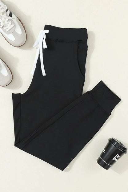 Black jogger pants with white drawstring, paired with sneakers and a coffee cup on a neutral background
