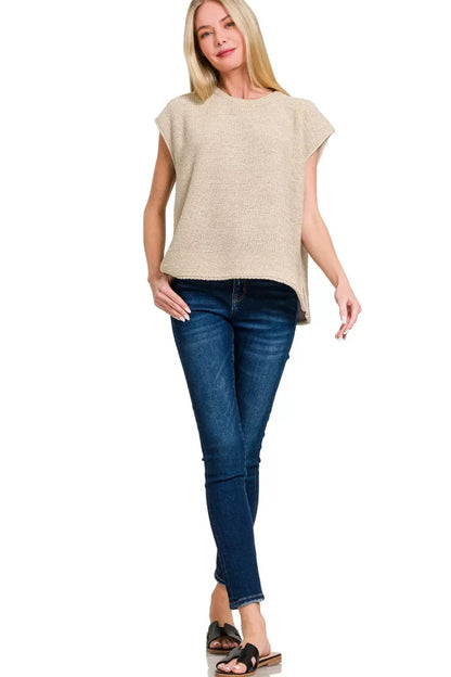 Woman wearing a beige knit sleeveless top with blue skinny jeans and black sandals