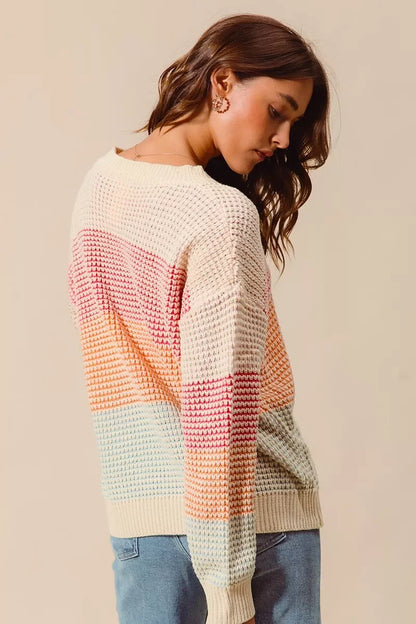Woman wearing a pastel color block knit sweater with relaxed fit and light wash jeans.