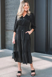 Woman wearing a black tiered midi dress with long sleeves, standing outdoors with a black handbag and sandals.