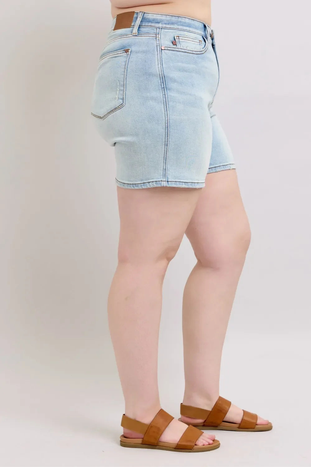 Woman wearing light wash denim shorts and brown sandals, side view