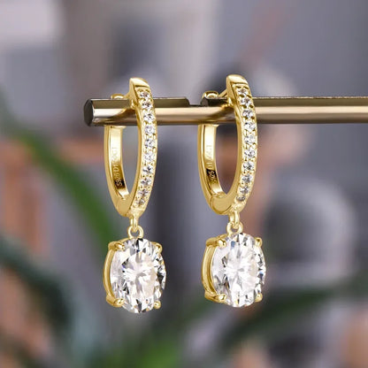 Gold hoop earrings with pavé crystals and large oval drop stones on a blurred background