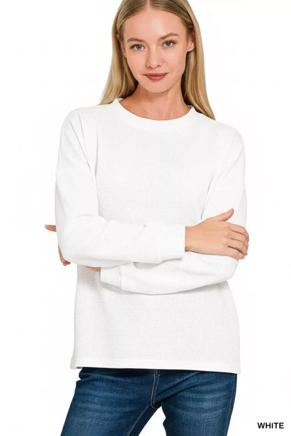 Woman wearing a white long sleeve knit top with crew neck and blue jeans, front view