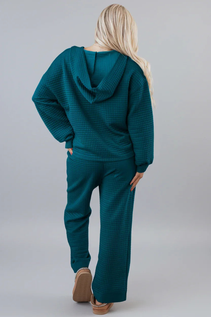 Woman wearing teal textured loungewear hoodie and pants set, standing with back facing camera