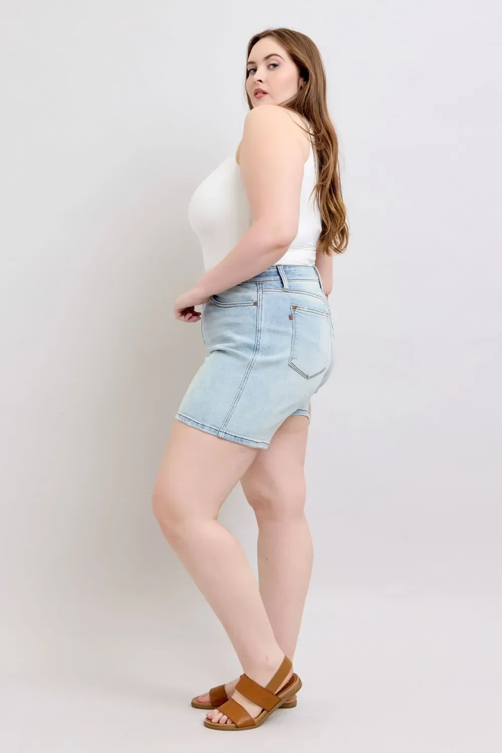 Woman in white tank top and high-waisted light blue denim shorts with brown sandals