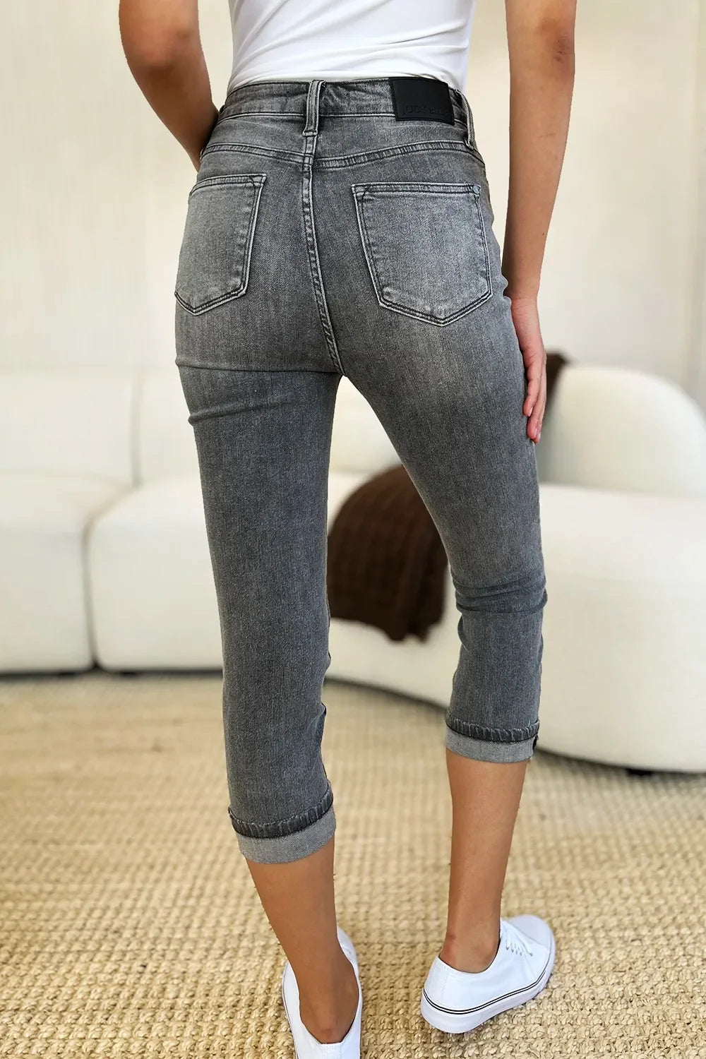 Woman wearing grey cropped skinny jeans with rolled cuffs and white sneakers in a modern living room