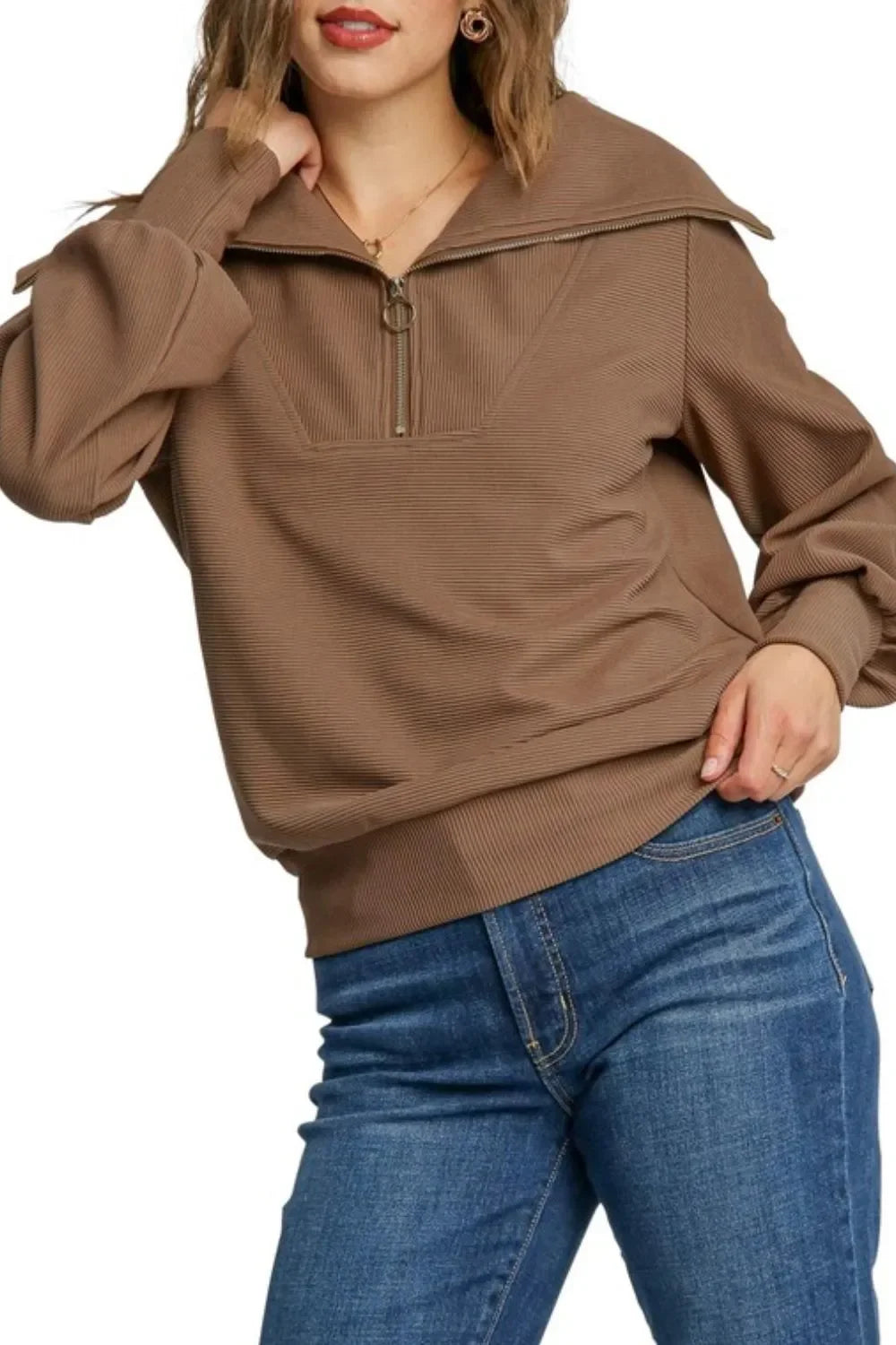 Woman wearing a brown ribbed pullover with half-zip collar and blue jeans