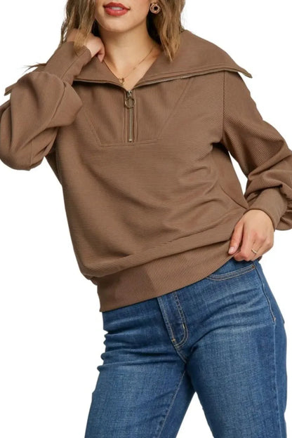 Woman wearing a brown ribbed pullover with half-zip collar and blue jeans