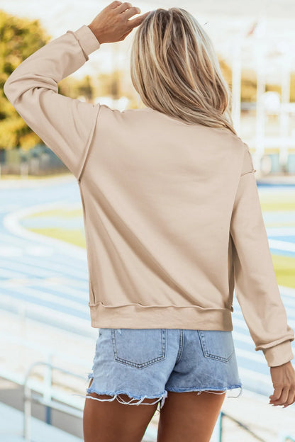 Woman in tan sweatshirt and denim shorts standing outdoors by a track field