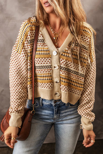 Woman wearing a patterned knit cardigan with button front, blue jeans, and layered necklaces.
