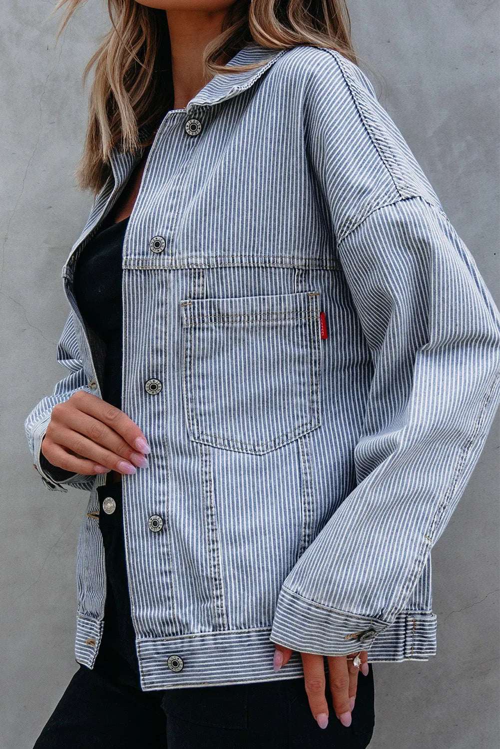 Woman wearing a relaxed fit, blue and white striped denim jacket with front pocket.