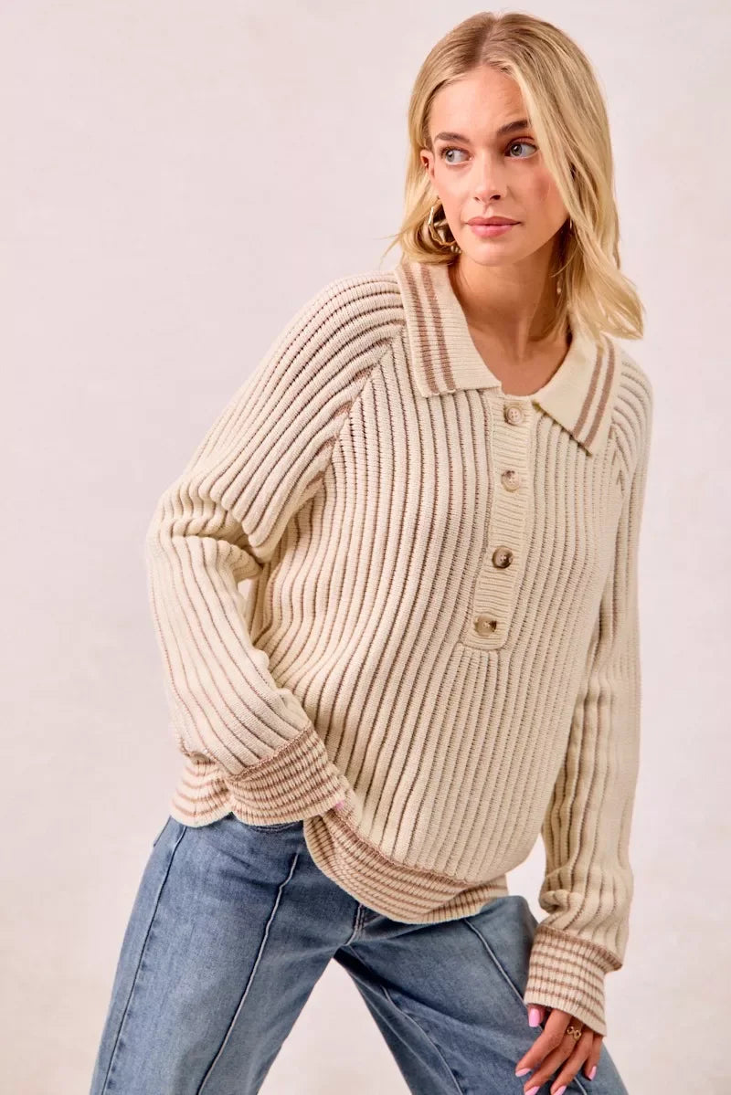Woman wearing a cream ribbed knit sweater with button front and collared neckline, paired with blue jeans