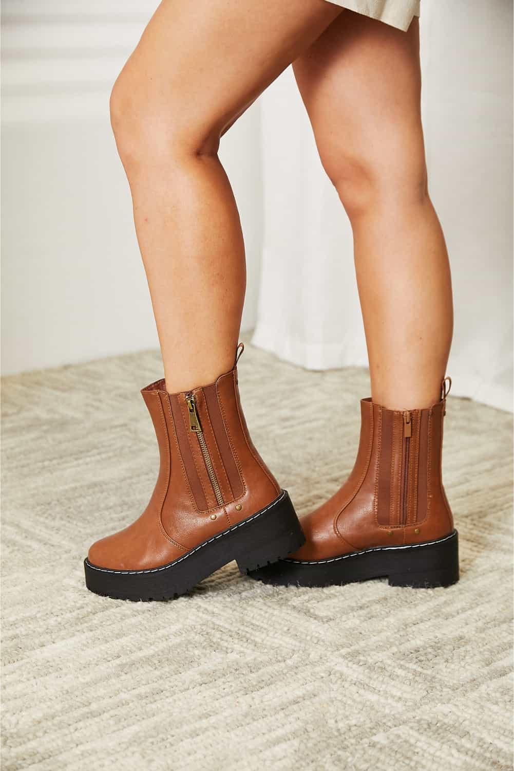 Woman wearing brown leather ankle boots with side zippers and black lug soles on carpet