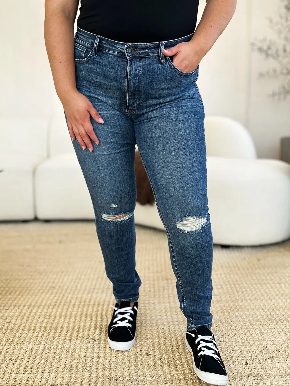 Woman wearing distressed blue skinny jeans and black sneakers in a modern living room