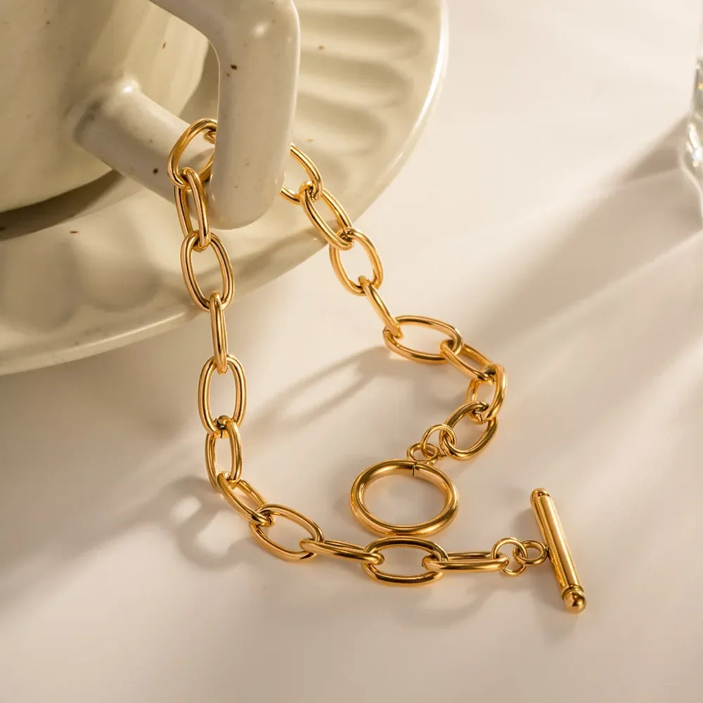 Gold chain link bracelet with toggle clasp on a cream ceramic mug, minimal jewelry
