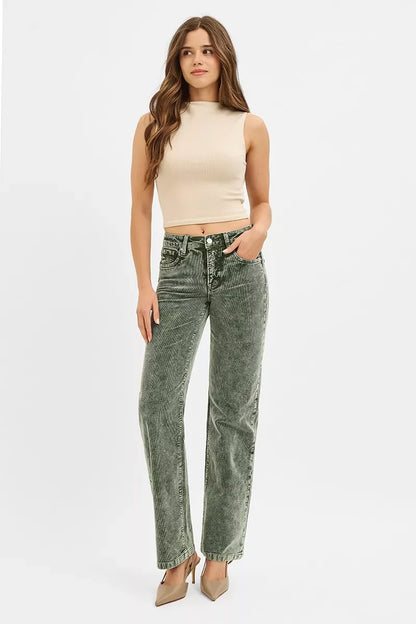 Woman in sleeveless beige crop top and green corduroy jeans, neutral heels, studio background