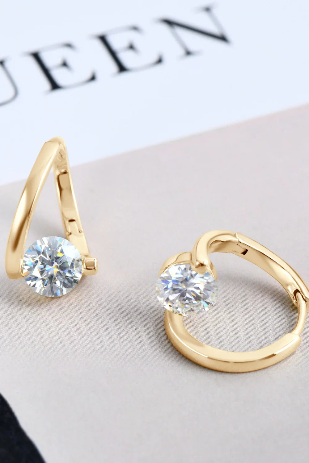 Gold hoop earrings with round clear gemstones on a neutral fabric background
