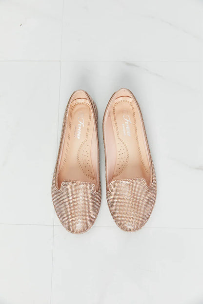 Pair of rose gold embellished loafers for women on a white marble background